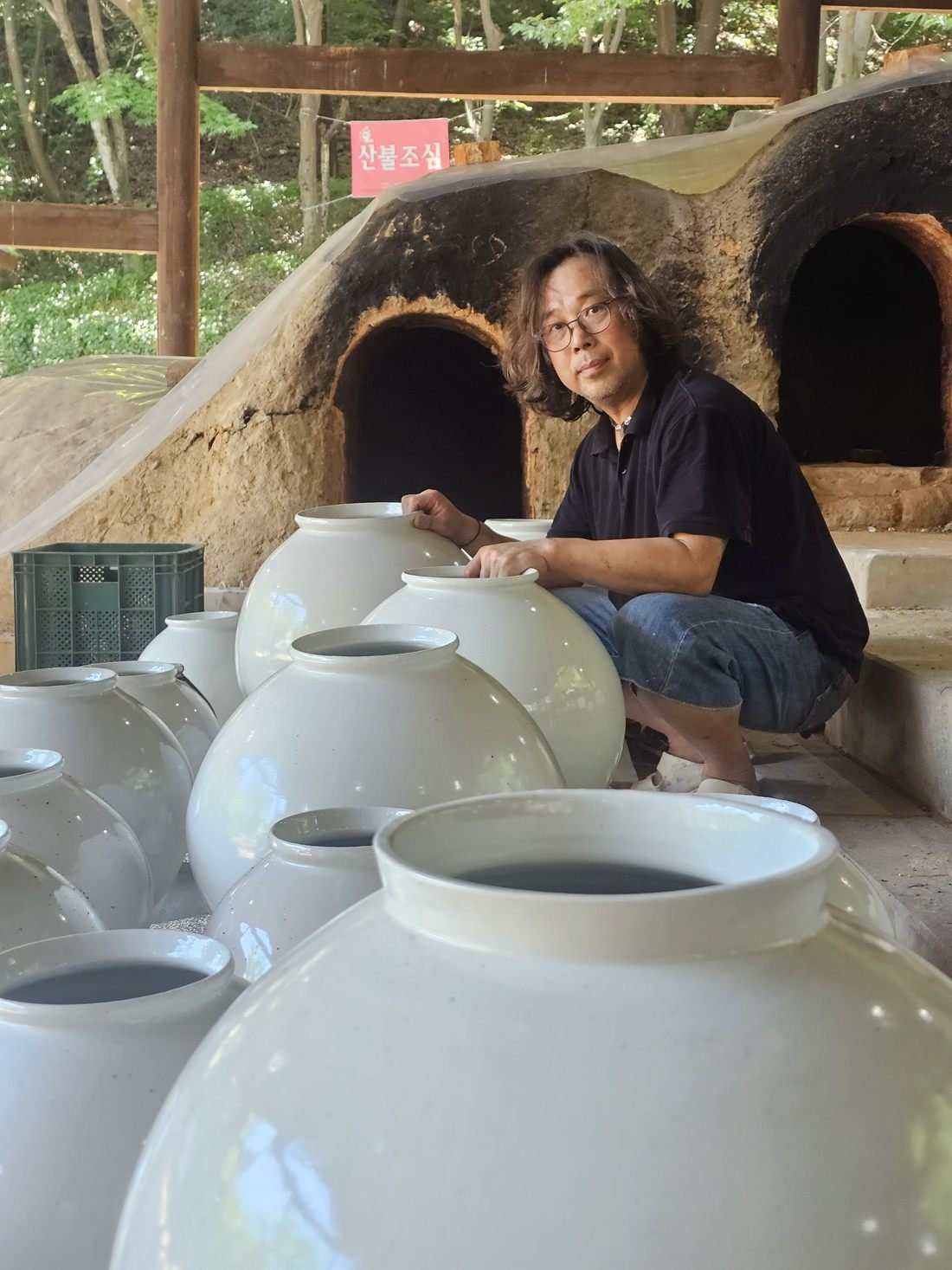 Shin Hyun Moon accroupi parmi des moon jars blancs émaillés, devant un four à bois traditionnel
